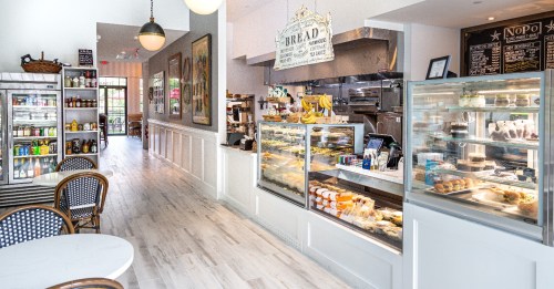 A bright café interior featuring a display case with pastries, a counter, and seating areas.