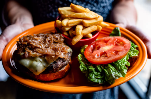 A plate with a burger topped with melted cheese and onions, served with fries, lettuce, and tomato slices.