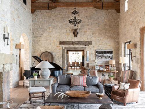 Spacious living room with stone walls, a grand piano, cozy seating, and rustic decor, featuring warm lighting and wooden beams.