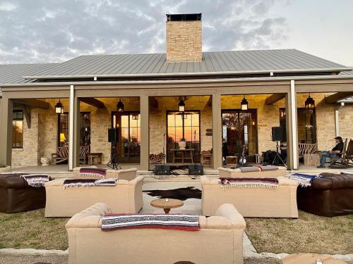 A cozy outdoor seating area with sofas and a view of a sunset behind a stone house with a chimney.