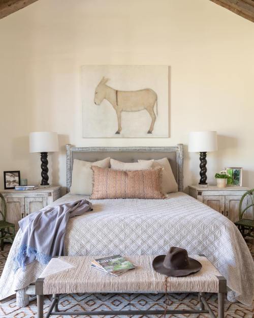 Cozy bedroom featuring a bed with a patterned quilt, side tables, lamps, and a donkey painting above the headboard.