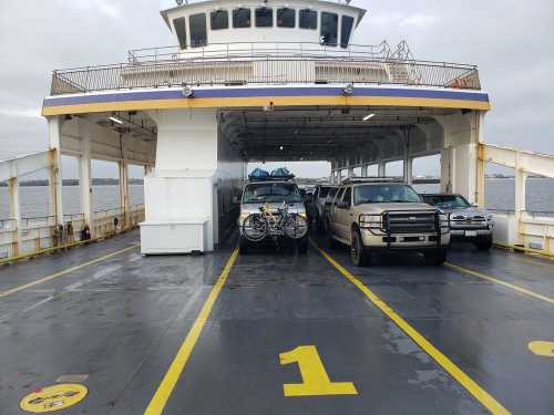 A ferry interior with parked vehicles, including a truck with a bike on the back, and another truck beside it.