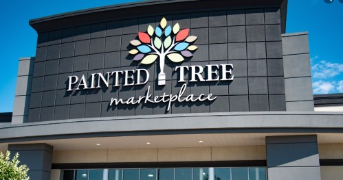 Sign for Painted Tree Marketplace featuring a colorful tree logo against a modern building facade.