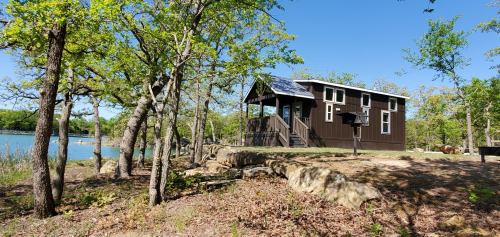 A small brown cabin surrounded by trees near a calm lake on a sunny day.