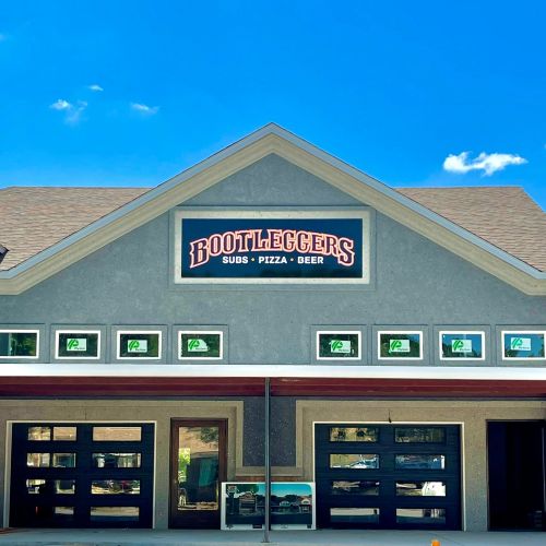 Exterior of a building with a sign reading "Bootleggers" and offerings of subs, pizza, and beer.