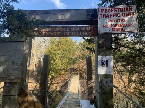 A wooden suspension bridge with signs indicating weight limits and pedestrian traffic only, surrounded by trees.