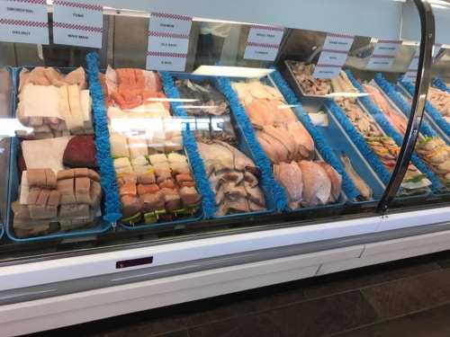 A display case filled with various types of fresh fish and seafood, neatly arranged on blue trays.