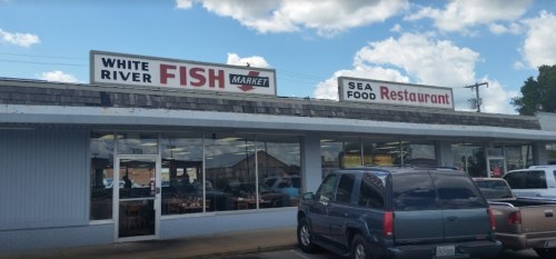 Exterior of White River Fish Market and Seafood Restaurant, featuring a sign and parked cars in front.