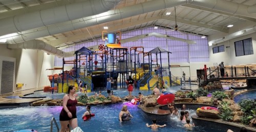 Indoor water park featuring a large play structure, water slides, and children swimming in a pool.