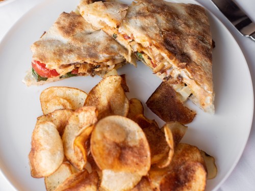 A plate with a grilled sandwich filled with vegetables and a side of crispy potato chips.