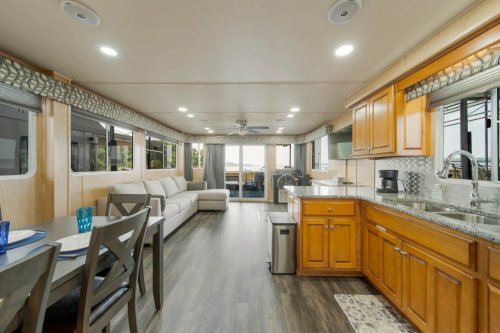 Interior of a modern RV featuring a kitchen, dining area, and living space with large windows and wooden cabinetry.