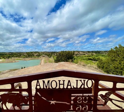 View from a lookout point with a metal sign reading "Oklahoma," overlooking a green landscape and blue sky.