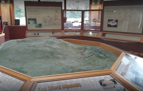 A display featuring a model of the Ward Mounds, surrounded by informational panels in a museum setting.