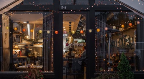 A cozy restaurant with warm lighting and decorative string lights, visible through large windows.