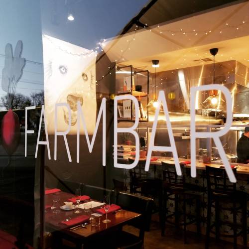 A restaurant window displaying the name "FARMBAR" with a cozy interior and warm lighting visible inside.