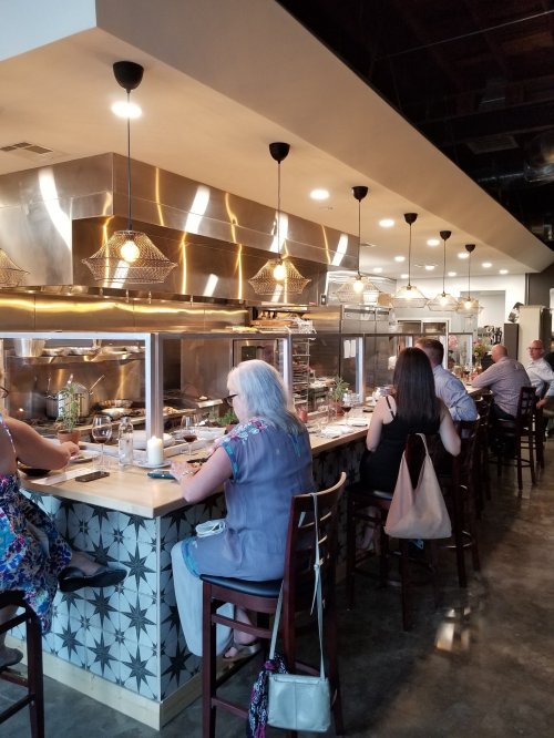 A modern restaurant interior with patrons seated at a counter, enjoying meals in a stylish, open kitchen setting.
