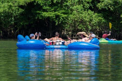 A group of people relaxes on a blue inflatable raft in a calm river surrounded by lush greenery.