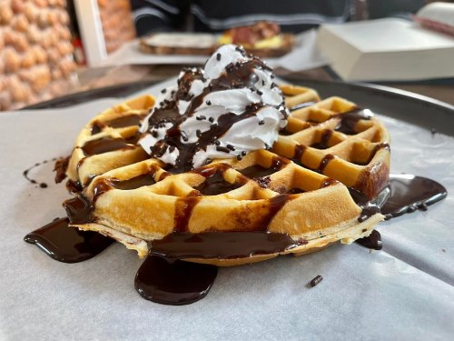 A close-up of a waffle topped with whipped cream and drizzled with chocolate sauce on a plate.