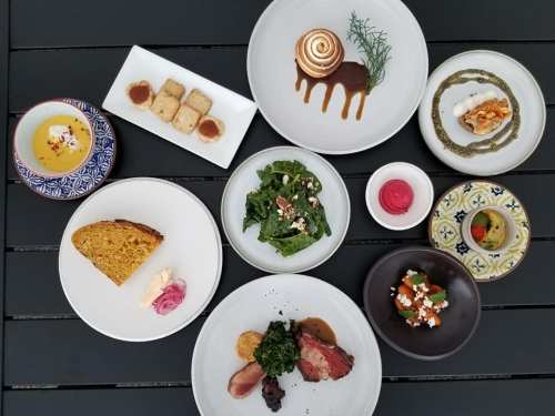 A variety of beautifully plated dishes, including desserts, salads, and meats, arranged on a dark table.