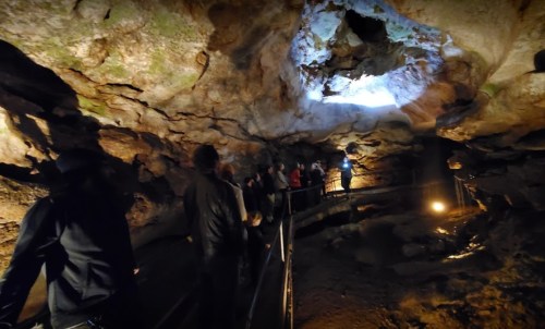 A group of people exploring a cave with rock formations and a light source from above.