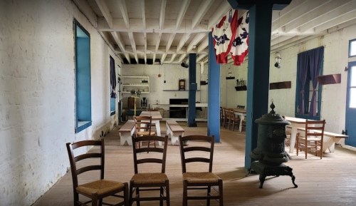 Interior of a rustic room with wooden chairs, long tables, and flags hanging from the ceiling.