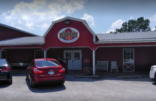 Red barn-style building with a sign reading "Peach Barn," featuring a parked car in front and a clear blue sky.