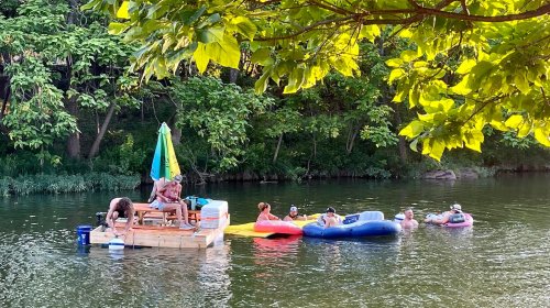 A group of people relax on floats and a wooden platform in a serene river surrounded by lush greenery.