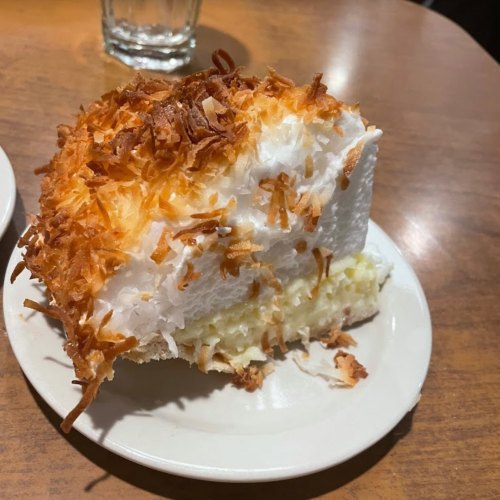 A slice of coconut cream pie topped with toasted coconut flakes on a white plate.