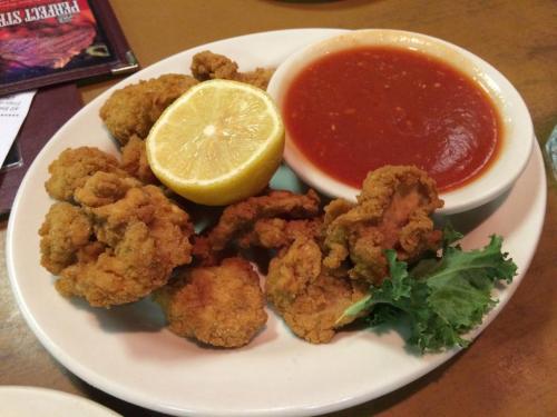 A plate of fried seafood with a lemon wedge, served alongside a bowl of marinara sauce and a garnish of kale.