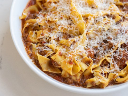 A bowl of pasta with meat sauce, topped with grated cheese and wide noodles.