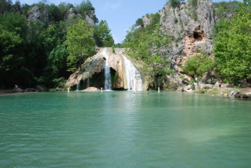 A serene waterfall cascades into a turquoise pool, surrounded by lush greenery and rocky cliffs.