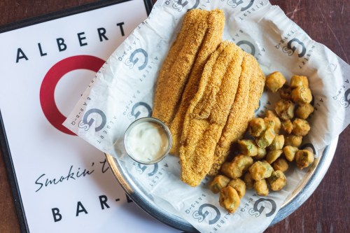 A plate of golden fried catfish fillets with a side of crispy okra and a small cup of dipping sauce.