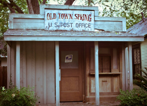 A rustic building with a sign reading "Old Town Spring U.S. Post Office," surrounded by trees.