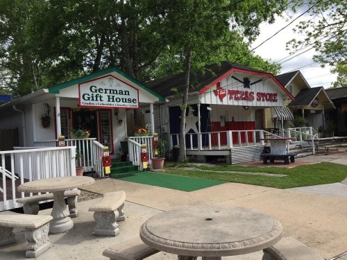 Two colorful shops, "German Gift House" and "Texas Store," with outdoor seating and greenery in the background.