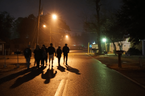 A group of people walking down a dimly lit street at night, with shadows cast by streetlights.