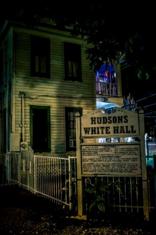A historic building at night, featuring a sign that reads "Hudsons White Hall" with a white picket fence.