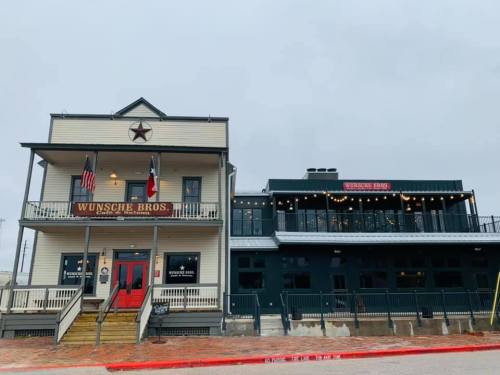 Historic building with a star emblem, featuring a porch, flags, and a modern addition with outdoor seating.