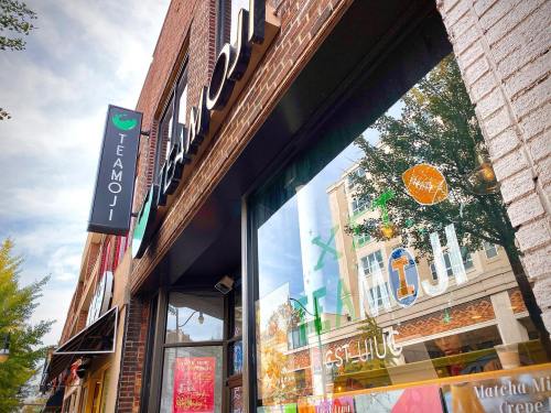 Exterior view of a café named "Teamoji," featuring a colorful sign and large windows showcasing the street outside.