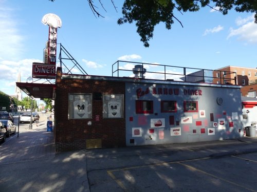 A retro diner with a red and white exterior, featuring a sign that reads "Red Arrow Diner" and cartoonish face decorations.