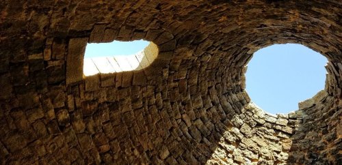 View looking up at a stone structure with two circular openings revealing a clear blue sky.