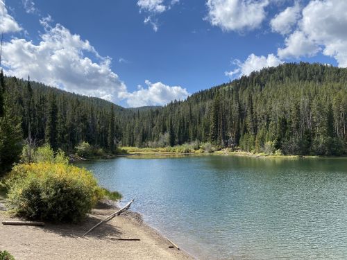 A serene lake surrounded by lush green trees and mountains under a partly cloudy sky.