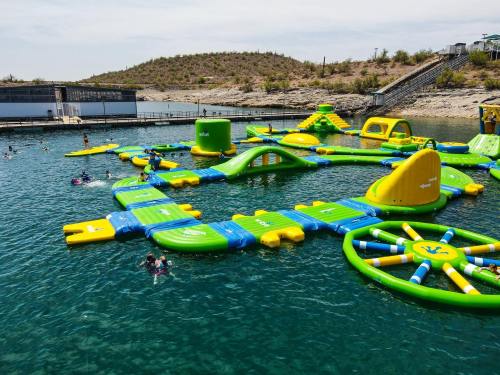 A colorful inflatable water park with various structures in a lake, surrounded by swimmers and hills in the background.