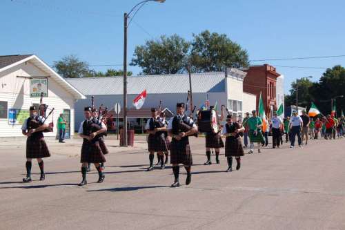 A parade featuring bagpipers in kilts, with flags and a crowd of spectators lining the street.