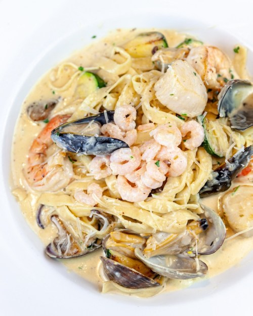 A creamy seafood pasta dish with shrimp, scallops, clams, and vegetables, garnished with herbs.
