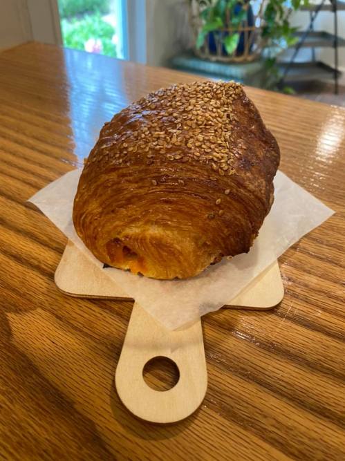 A golden-brown croissant topped with sesame seeds, resting on a wooden serving board.