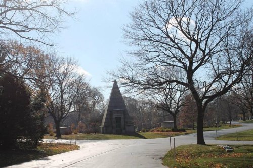 A pyramid-shaped structure surrounded by bare trees and a clear blue sky in a park setting.