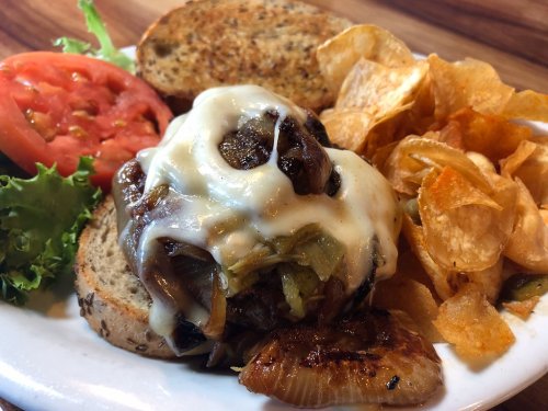 A juicy burger topped with melted cheese and sautéed onions, served with lettuce, tomato, and crispy potato chips.