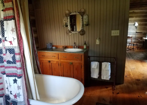 A rustic bathroom featuring a vintage bathtub, wooden cabinets, a mirror, and towels on a rack.