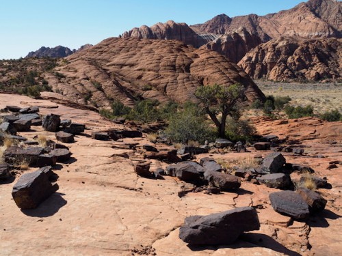A rocky landscape with layered hills and scattered boulders under a clear blue sky.