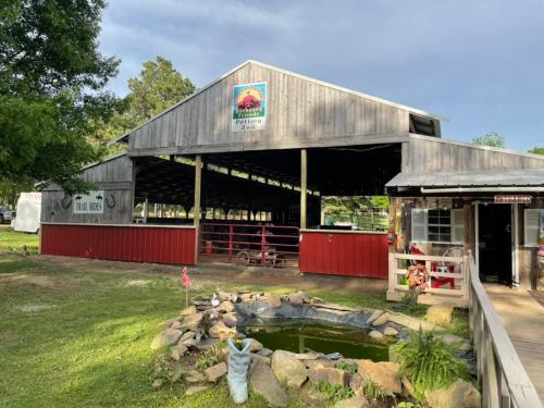 A rustic barn with a red lower section, surrounded by greenery and a small pond, under a cloudy sky.